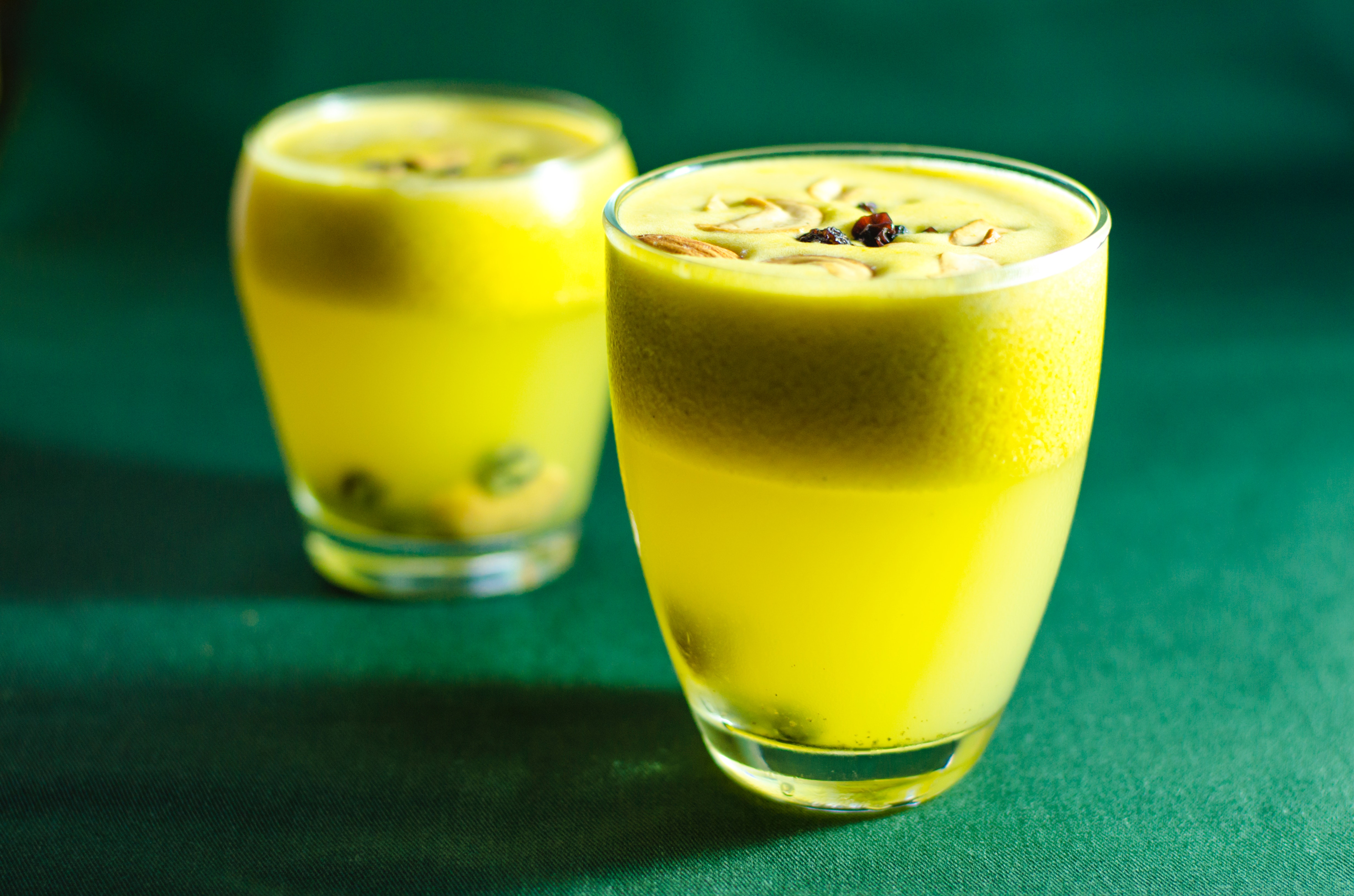 Two cocktailglasses filled with a yellow drink on a green table.