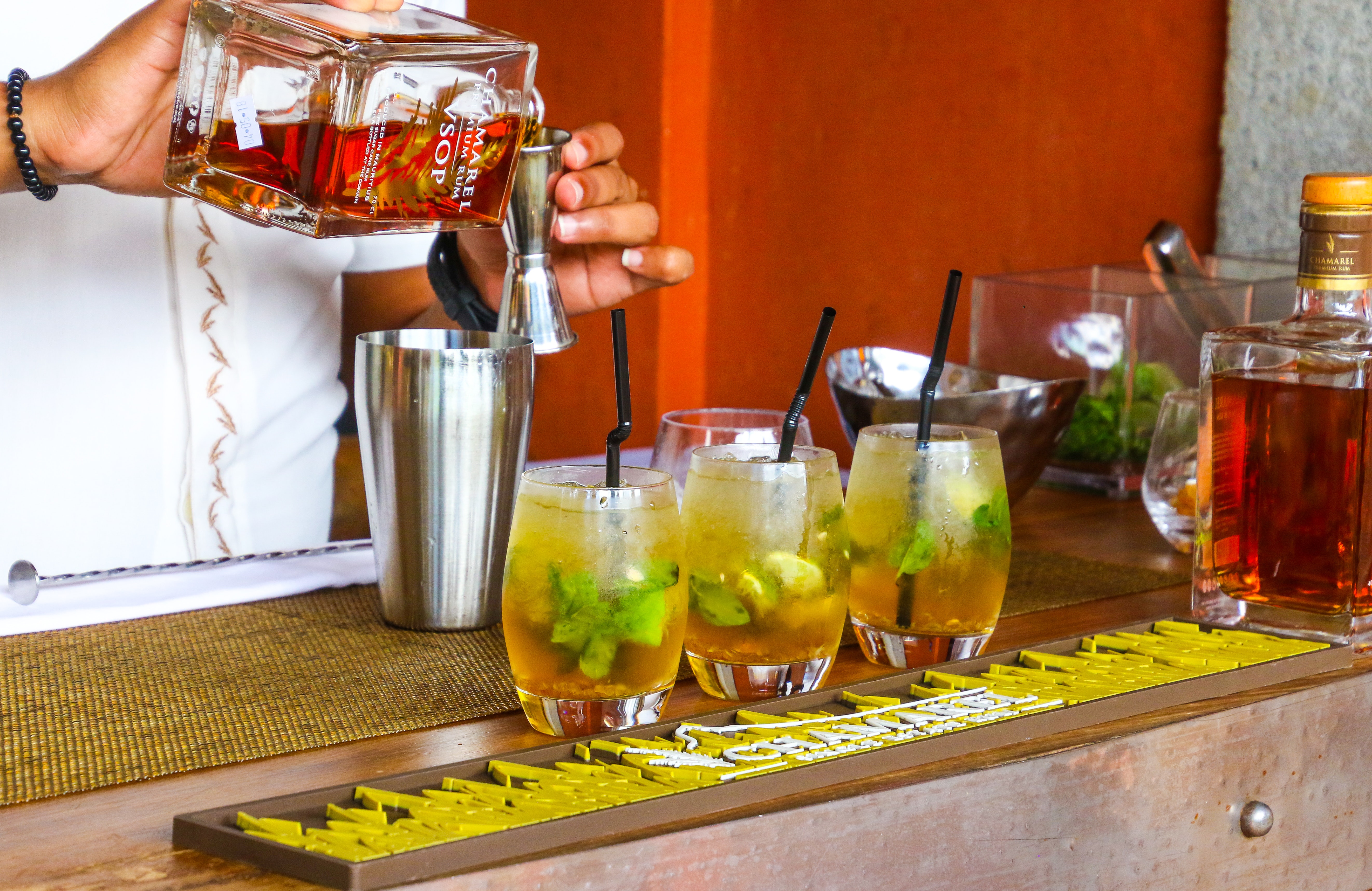Three drinks on the bar. Bartender mixing another drink in the Backround.